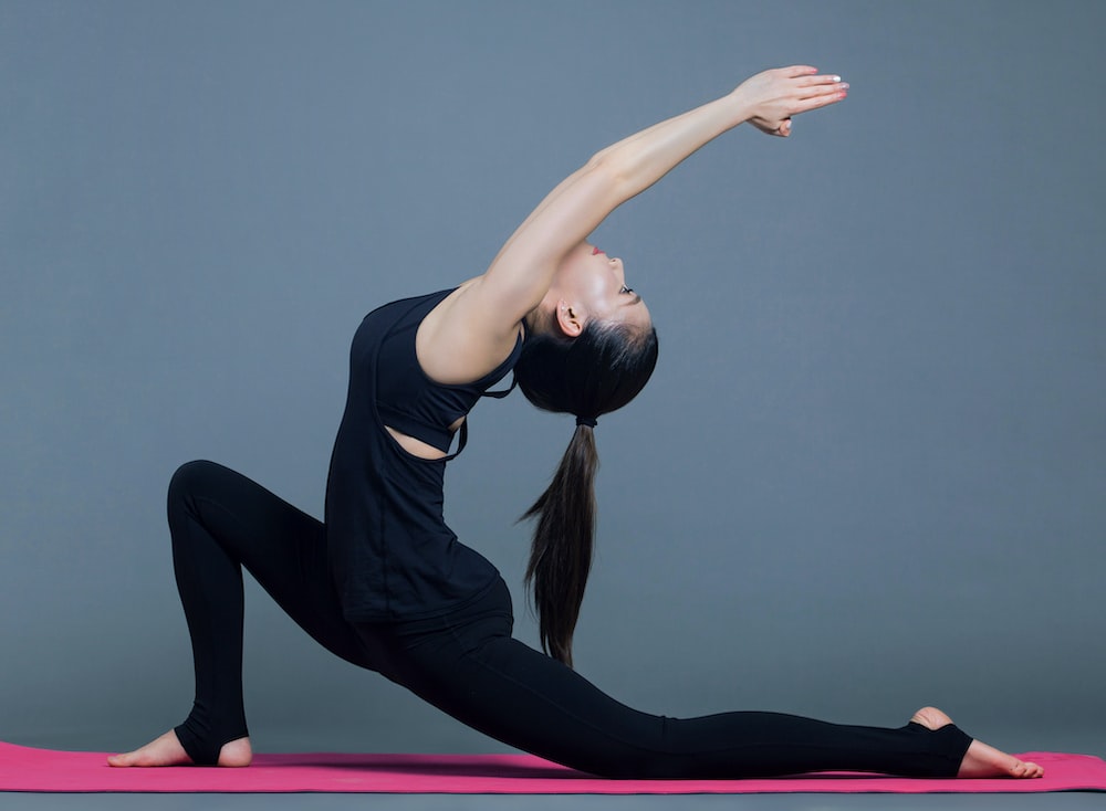 A Woman Striking a Yoga Pose with One Leg and Both Arms Stretched Back and the Other Leg Bent Forward