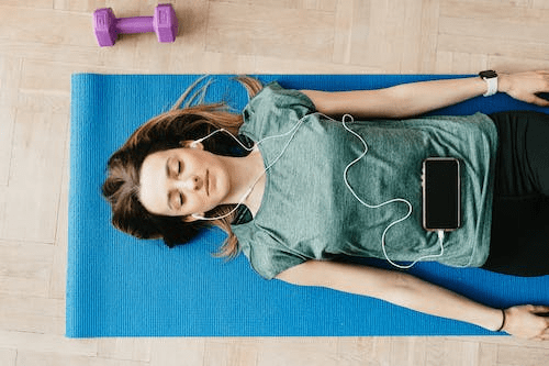 A woman lying down on her yoga mat while listening to music